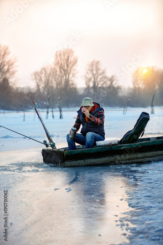Fisherman in winter fishing drink tea on frozen lake