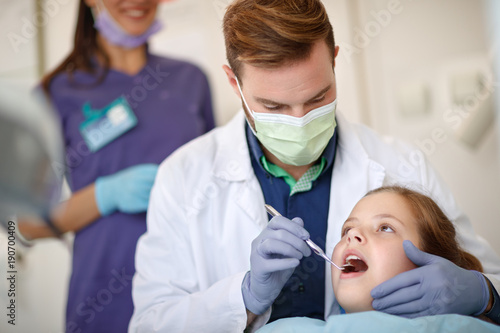 Male dentist looking with dental mirror child's teeth