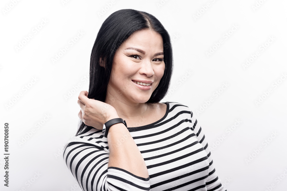 Useful technology. Pretty dark-haired woman in a striped pullover posing for the camera and raising her hand as if showing her fitness tracker on the wrist Useful technology. Pretty dark-haired woman in a striped pullover posing for the camera and raising her hand as if showing her fitness tracker on the wrist
