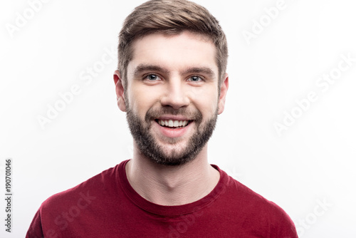 Attractive male. Close up of a handsome upbeat young man in a burgundy t-shirt smiling at the camera while posing isolated on a white background