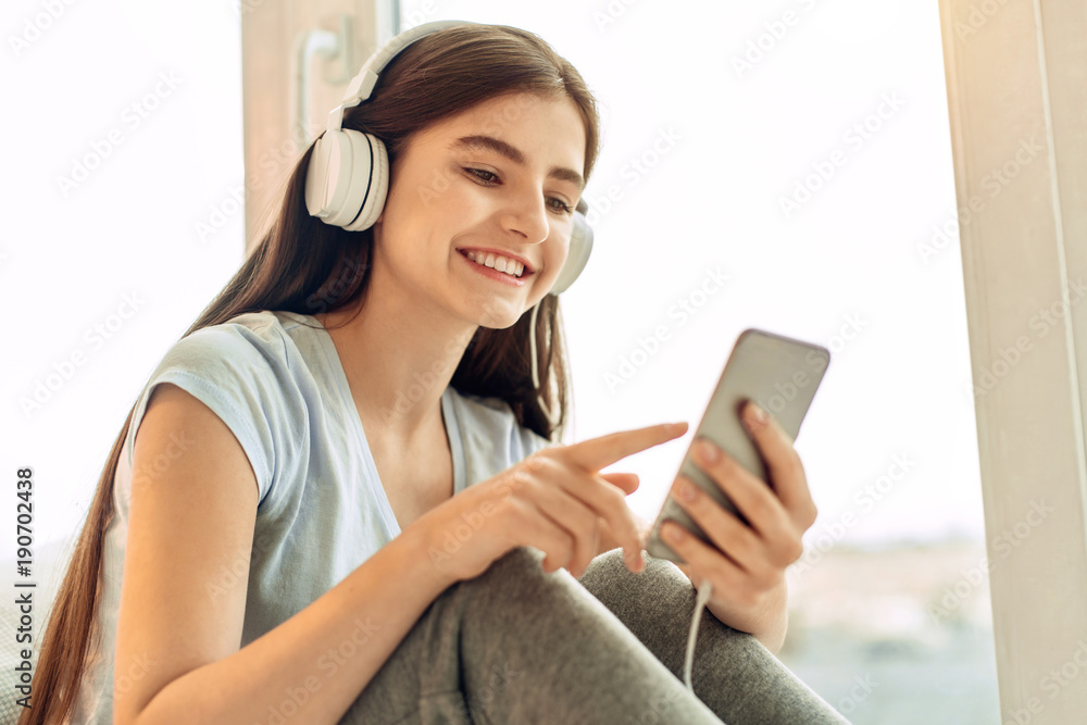 Best music. Beautiful teenage girl scrolling her playlist and choosing the songs to play while listening to the music in the headphones and smiling Best music. Beautiful teenage girl scrolling her playlist and choosing the songs to play while listening to the music in the headphones and smiling