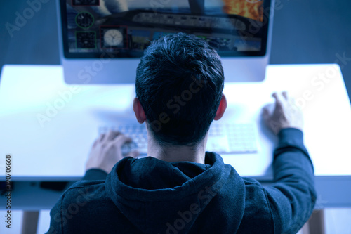 New level. Top view of confident strong male gamer sitting with back to the camera while completing level and putting hands on keyboard and mouse