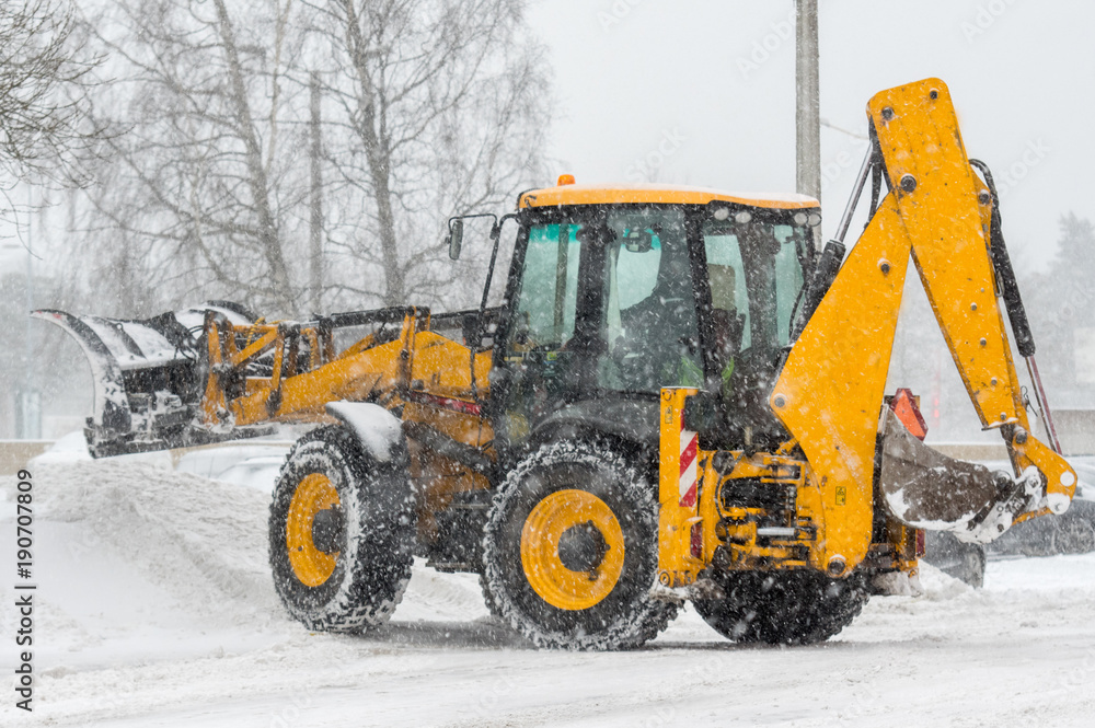 Yellow tractor with snowplow removing snow during heavy snowfall. Winter time street maintenance in hard weather conditions. Yellow tractor with snowplow removing snow during heavy snowfall. Winter time street maintenance in hard weather conditions.