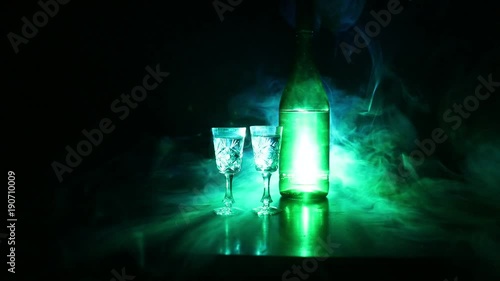 Two glasses of Vodka with bottle on dark foggy club style background with glowing lights (Laser, Stobe) Multi colored. Club drinks theme decoration. Empty space. Selective focus photo