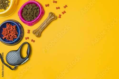 Dry dog food in bowl and pet accessories on yellow background top view. Pet feeding concept backgrounds with copy space. Frame composition.