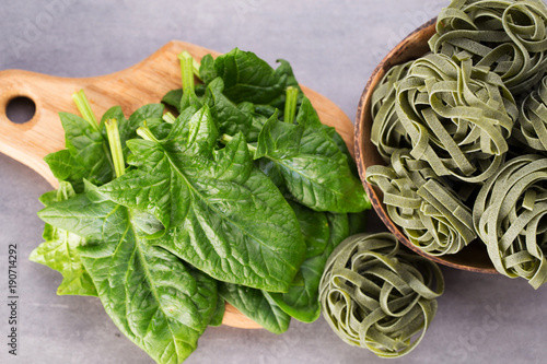 Fresh spinach with green pasta on a gray background.