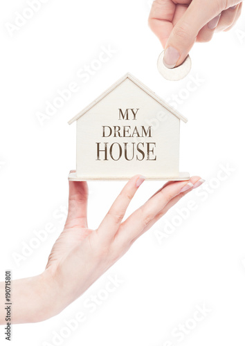 Female hand holding wooden house model with coin