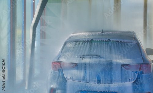 Small sedan travelling through a water jet car wash with foam and water being sprayed