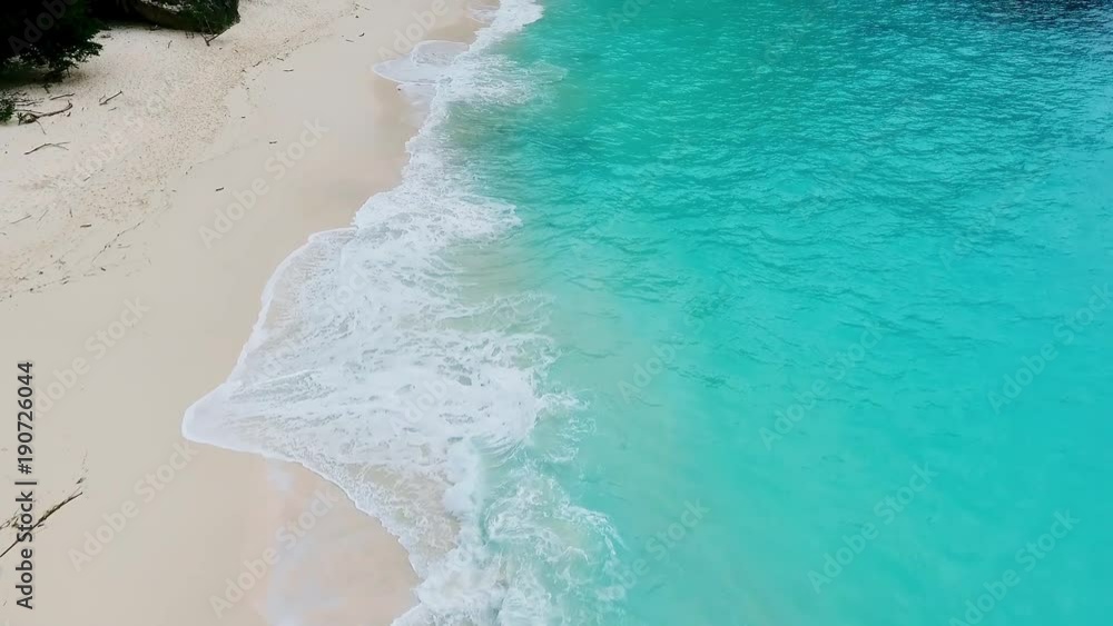 Ocean wave on tropical beach. White sand and crystal-blue sea. Aerial view