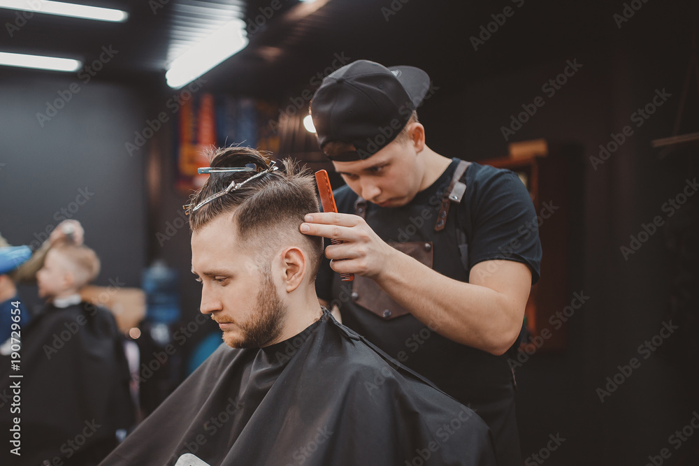 Barber shop. Master cuts hair and beard of men in barbershop, hairdresser makes hairstyle for young man Barber shop. Master cuts hair and beard of men in barbershop, hairdresser makes hairstyle for young man