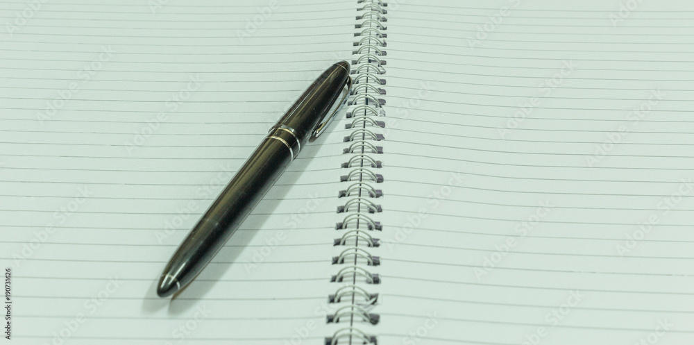 Image depicting blank spiral notebook with a black vintage pen placed over for financial investments or calculation. With selective focus on the subject. Image depicting blank spiral notebook with a black vintage pen placed over for financial investments or calculation. With selective focus on the subject.