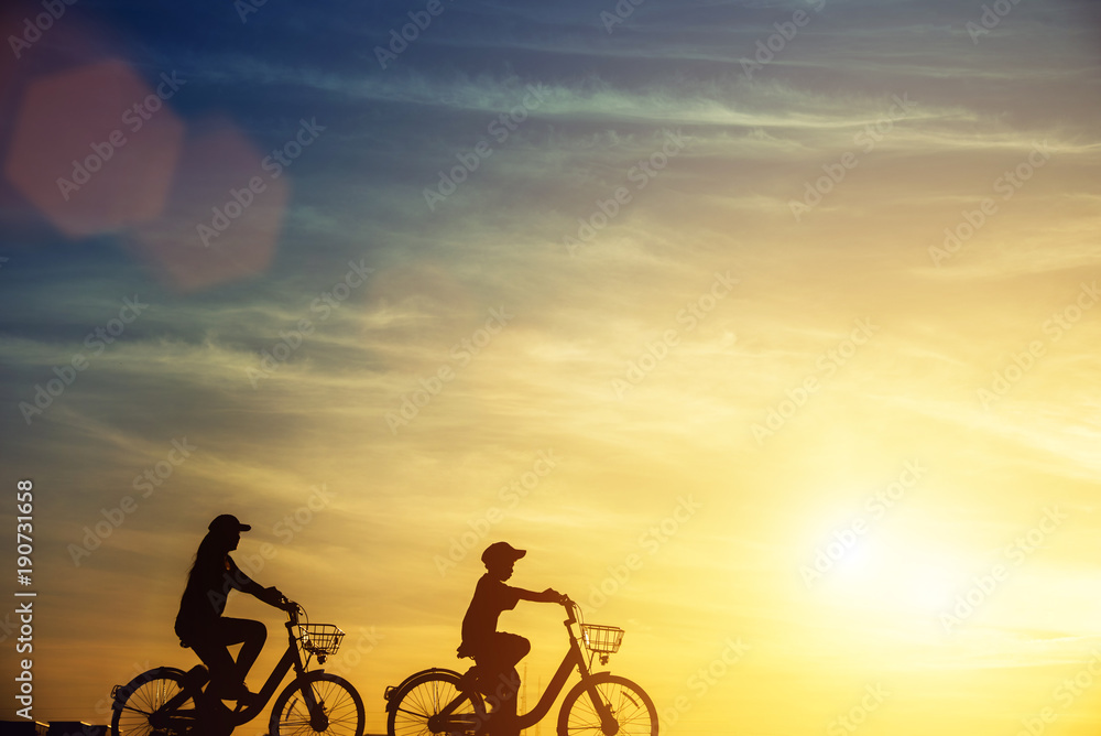 Mother and son having fun riding bike at sunset, active family sport, active kids sport