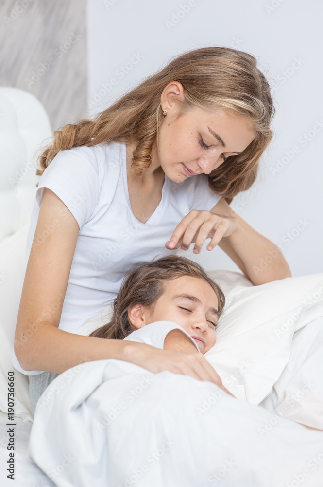 Happy young mom stroking her daughter on the bed Happy young mom stroking her daughter on the bed