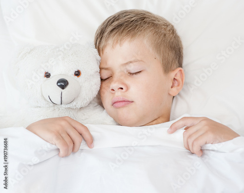 Sad boy sleeping in bed with toy bear. Top view