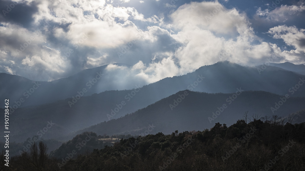 Mountain silhouettes on a cloudscape with rays of sun through the clouds Mountain silhouettes on a cloudscape with rays of sun through the clouds
