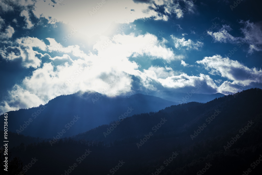 Mountain silhouettes on a cloudscape with rays of sun through the clouds