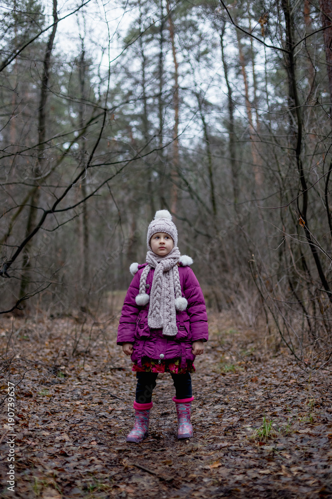 A little girl is standing in a forest on a path. A little girl is standing in a forest on a path.