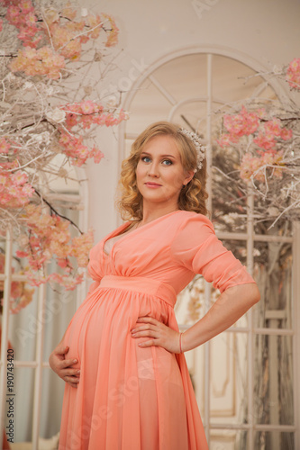 beautiful pregnant woman in anticipation of a child. Beautiful interior with flowers. Pregnant woman in peach dress © izida1991