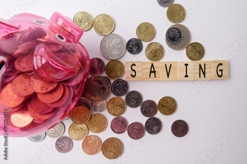 SAVING CONCEPT. Red piggy bank and coins with word SAVING on wooden plates.