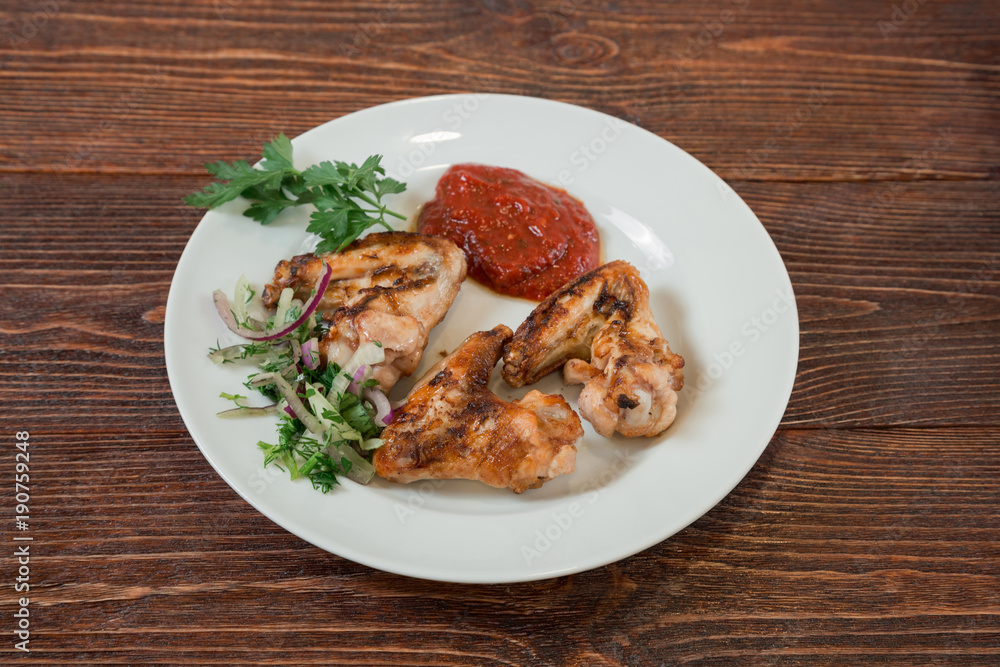 Roasted chiken wings on a plate. Appetizing dish on the wooden brown table. Roasted chiken wings on a plate. Appetizing dish on the wooden brown table.