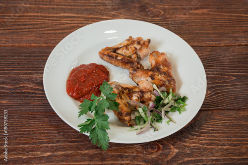 Roasted chiken wings on a plate. Appetizing dish on the wooden brown table.