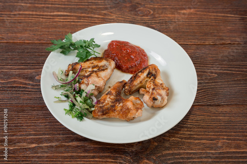 Roasted chiken wings on a plate. Appetizing dish on the wooden brown table.