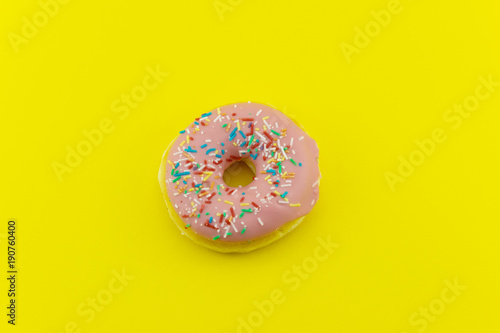 Close-up of a pink glazed donut isolated on yellow background. Strong candy contrast.