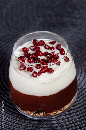 Chocolate avocado pudding on homemade granola bed, topped with banana whipped cream, garnished with juicy pomegranate seeds