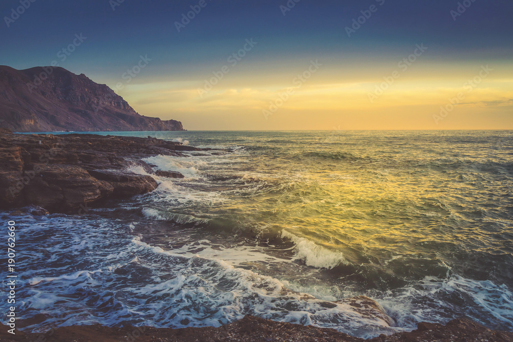The raging sea on the mountain coast at sunset