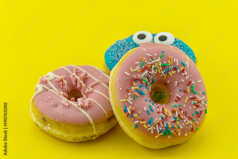 Close-up with many multicolored glazed donuts on yellow background. Close-up with many multicolored glazed donuts on yellow background.