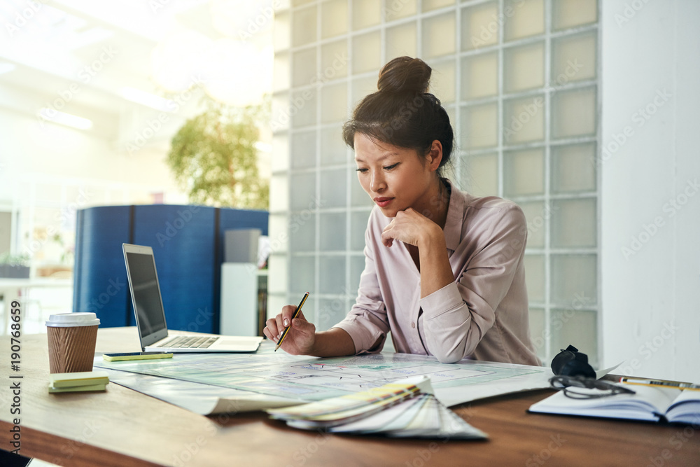 Young female architect working on blueprints in an office Young female architect working on blueprints in an office