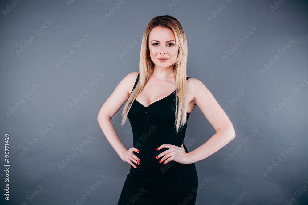 Beautiful woman with blond hair in the studio on a dark background in a black dress posing for us Beautiful woman with blond hair in the studio on a dark background in a black dress posing for us