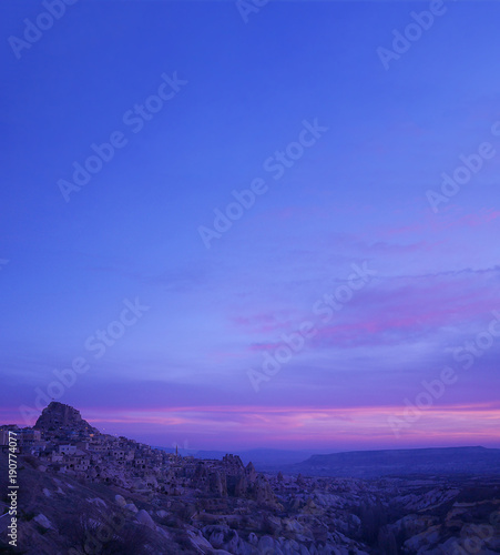 Purple sky during sunrise over Uchisar Castle and rocky village of Cappadocia, a historical region in Central Anatolia, Turkey. Uchisar is the highest point in Cappadocia, on the Nevsehir-Goreme road