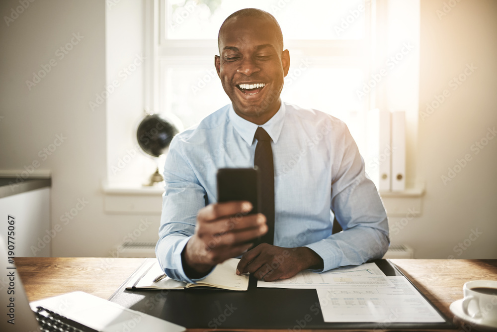 Smiling young businessman laughing at a cellphone message Smiling young businessman laughing at a cellphone message