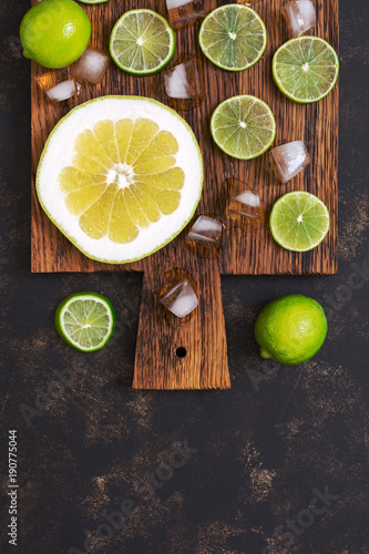 Slices of lime and pomelo with ice on a cutting board, dark background.