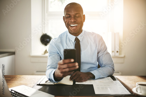 Smiling young businessman laughing at a cellphone message