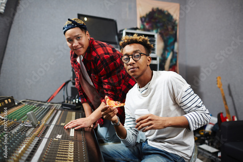 Man with pizza and drink and his colleague spending working day in sound recording studio