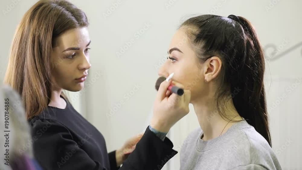 Visagist doing makeup for model with brush in beauty salon, toning skin Visagist doing makeup for model with brush in beauty salon, toning skin