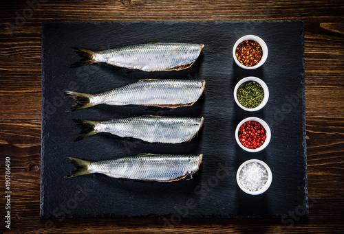 Fresh raw herrings with herbs served on black stone