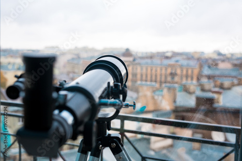 Professional telescope of black color by window with urban scene behind it