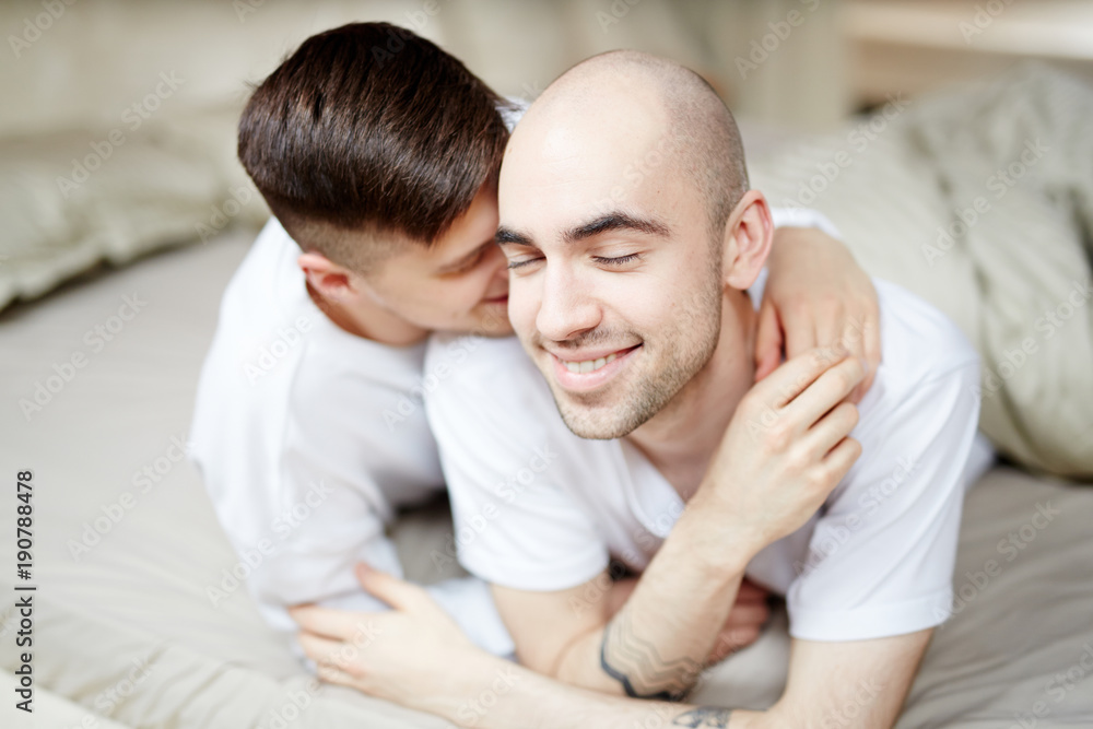 Young gay man enjoying embrace of his lover while relaxing on bed Young gay man enjoying embrace of his lover while relaxing on bed