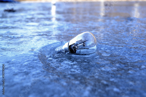 Light bulb in the ice. Electricity lamp on the ice background.