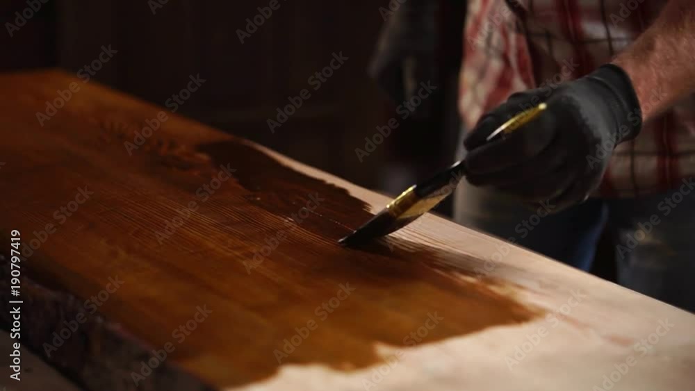 Experienced carpenter is applying fresh varnish on a grinded wooden table in a workshop. Applying all over the surface. Experienced carpenter is applying fresh varnish on a grinded wooden table in a workshop. Applying all over the surface.
