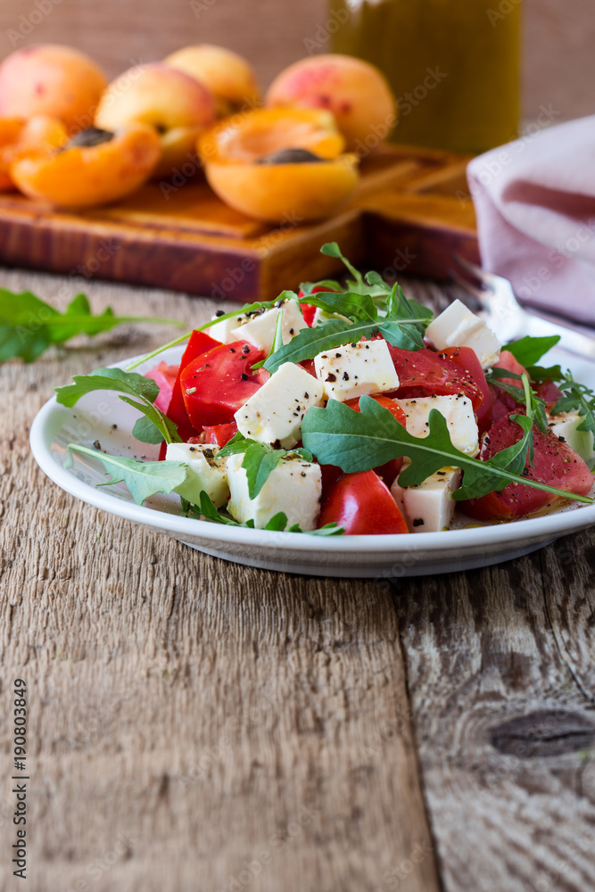 Feta arugula salad with tomatoes on white plate, summer food Feta arugula salad with tomatoes on white plate, summer food
