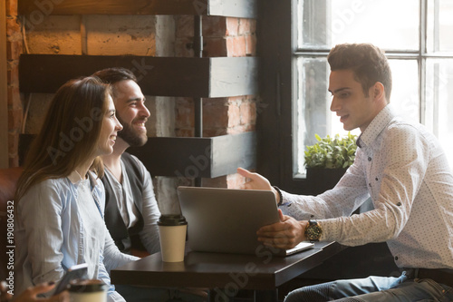 Insurance broker or salesman making offer to young millennial couple using laptop in cafe, realtor consulting customers about mortgage sitting at coffeehouse table pointing on computer screen photo