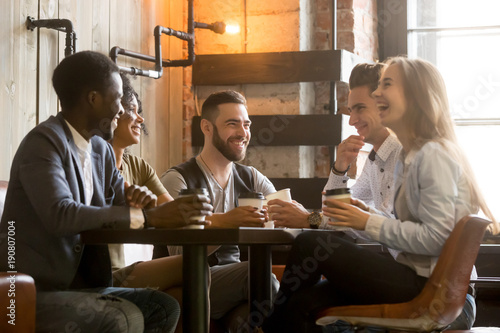 Multiracial friends having fun and laughing drinking coffee in coffeehouse, diverse young people talking joking sitting together at cafe table, multi ethnic millennials spending time in coffee shop photo