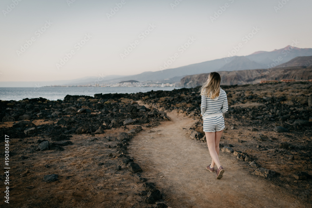 Girl walking through the desert not far from the ocean in the evening Girl walking through the desert not far from the ocean in the evening