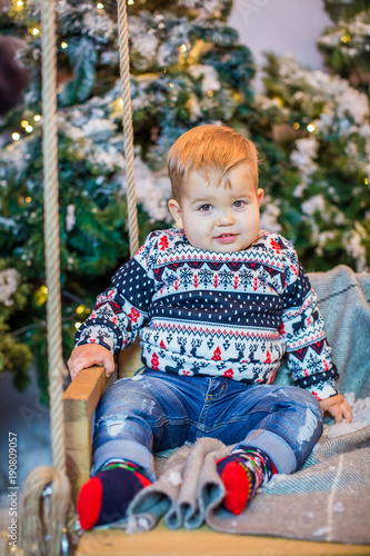 Little beautiful boy in sweater, sitting on a swing in winter
