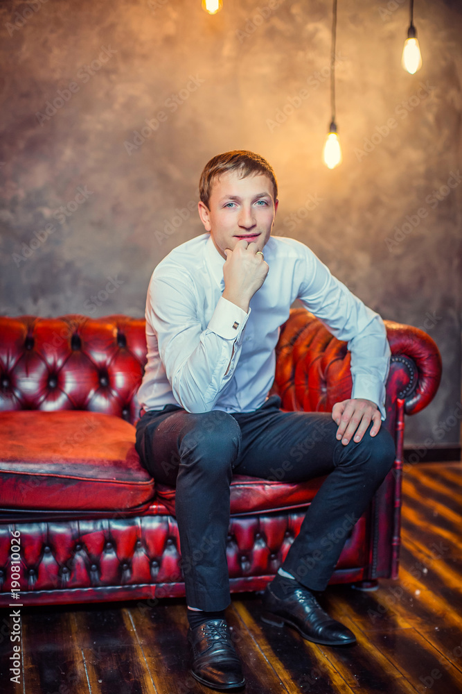 Obraz premium Stylish man in white shirt , sitting in leather red sofa