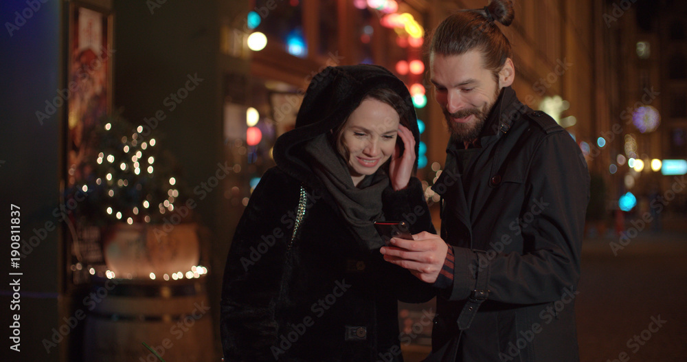 Young happy couple using smartphone at night. Young beautiful couple share memories and pictures on social media with online mobile app.